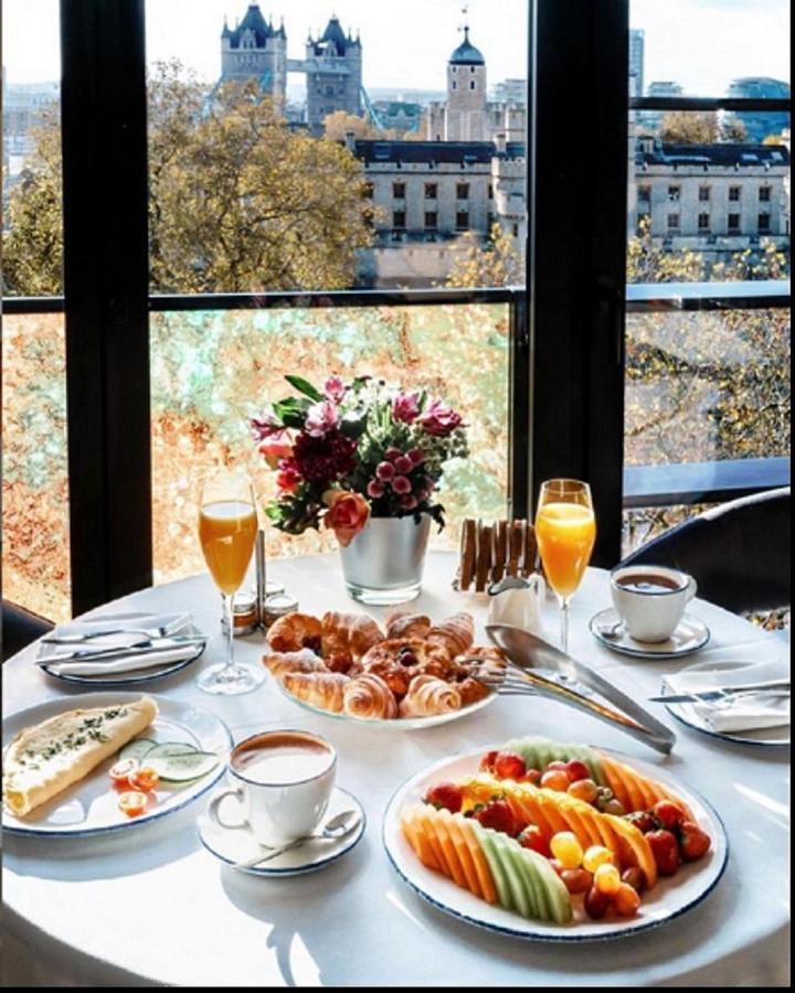 Tower Suites By Blue Orchid Лондон Екстер'єр фото The photo showcases a beautifully set breakfast table with a scenic view through large glass windows. The table features an array of items, including:

1. A small vase filled with colorful flowers.
2. Two glasses of orange juice.
3. A cup of coffee o