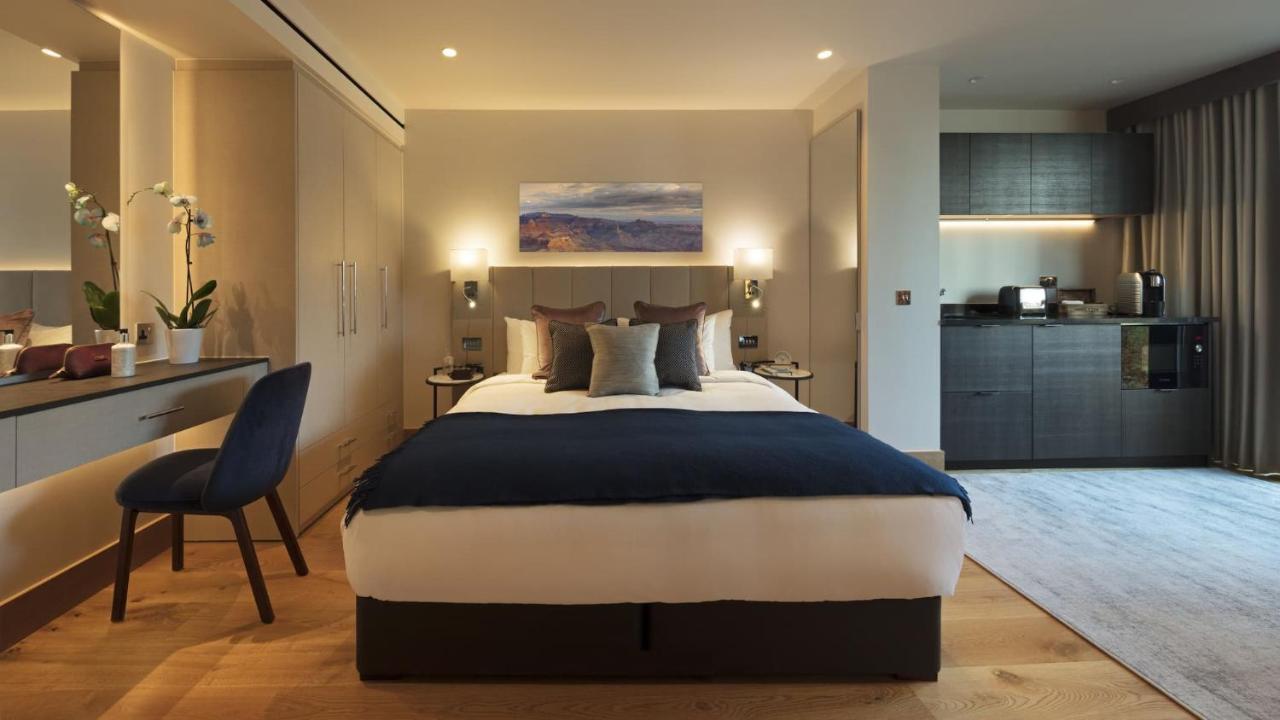 Tower Suites By Blue Orchid Лондон Екстер'єр фото The photo displays a modern hotel room featuring a plush bed with a dark blue bedspread and several decorative pillows. The walls are adorned in neutral tones, and there is a piece of artwork above the bed depicting a serene landscape. On the side, t