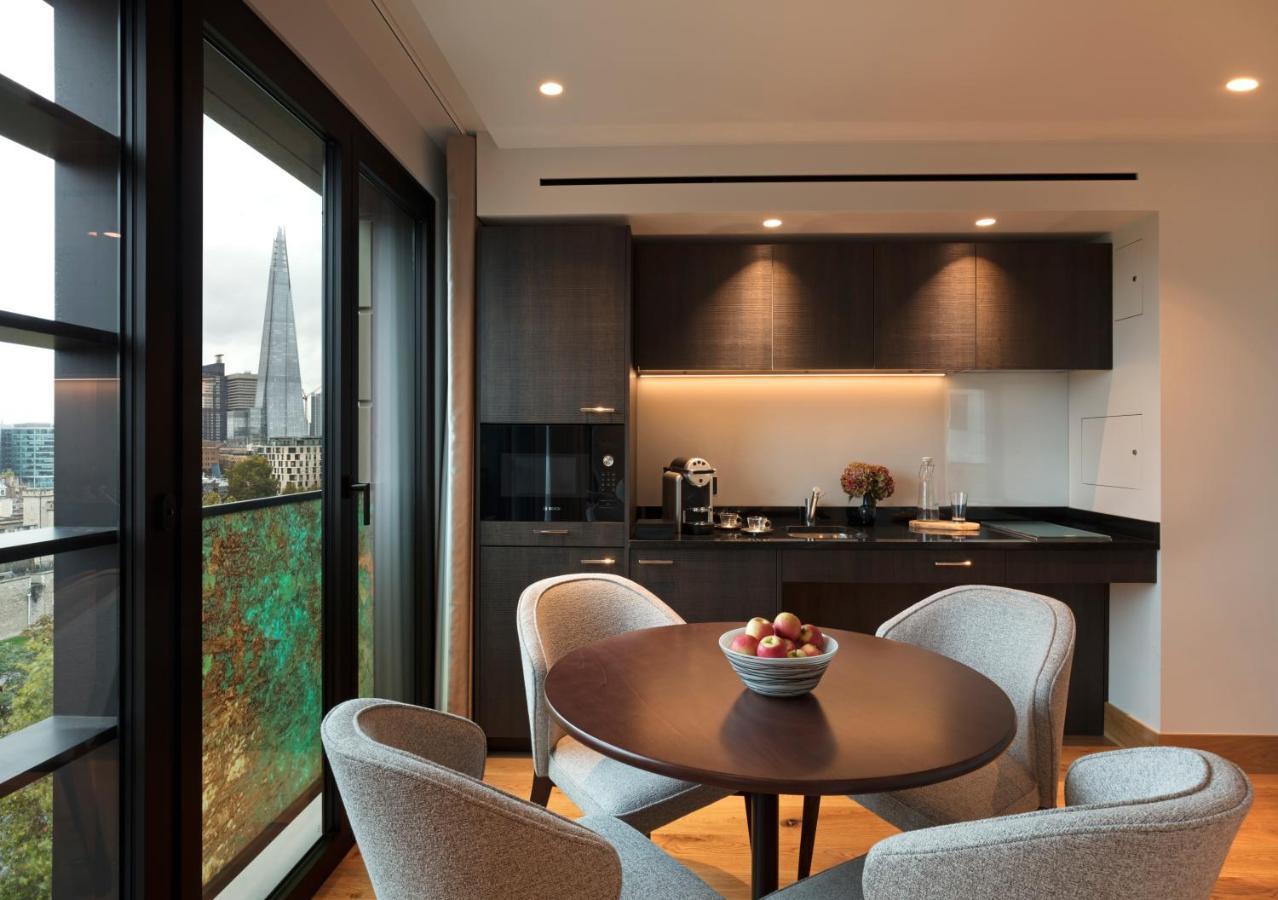 Tower Suites By Blue Orchid Лондон Екстер'єр фото The photo shows a modern kitchen and dining area. It features a round table with four gray chairs, and a bowl of apples is placed in the center of the table. The kitchen has dark cabinetry, a black countertop, and built-in appliances. Large windows a