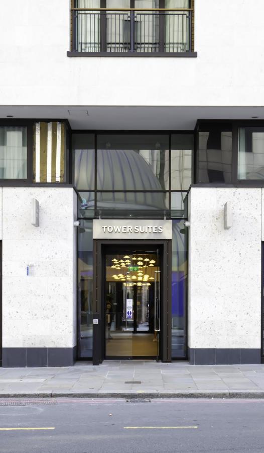 Tower Suites By Blue Orchid Лондон Екстер'єр фото The photo shows the entrance of a building labeled "TOWER SUITES." The entrance features large glass doors, allowing visibility into the interior. The building has a modern architectural style, with a light-colored stone facade and some decorative el