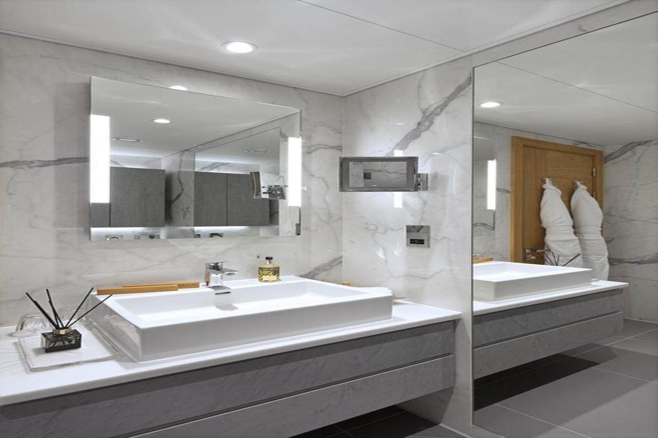 Tower Suites By Blue Orchid Лондон Екстер'єр фото The photo shows a modern bathroom featuring a sleek design. 

- **Vanity Area**: There is a rectangular sink set into a white countertop, paired with a minimalist faucet. 
- **Mirrors**: Above the sink, there is a large mirror that reflects the entir